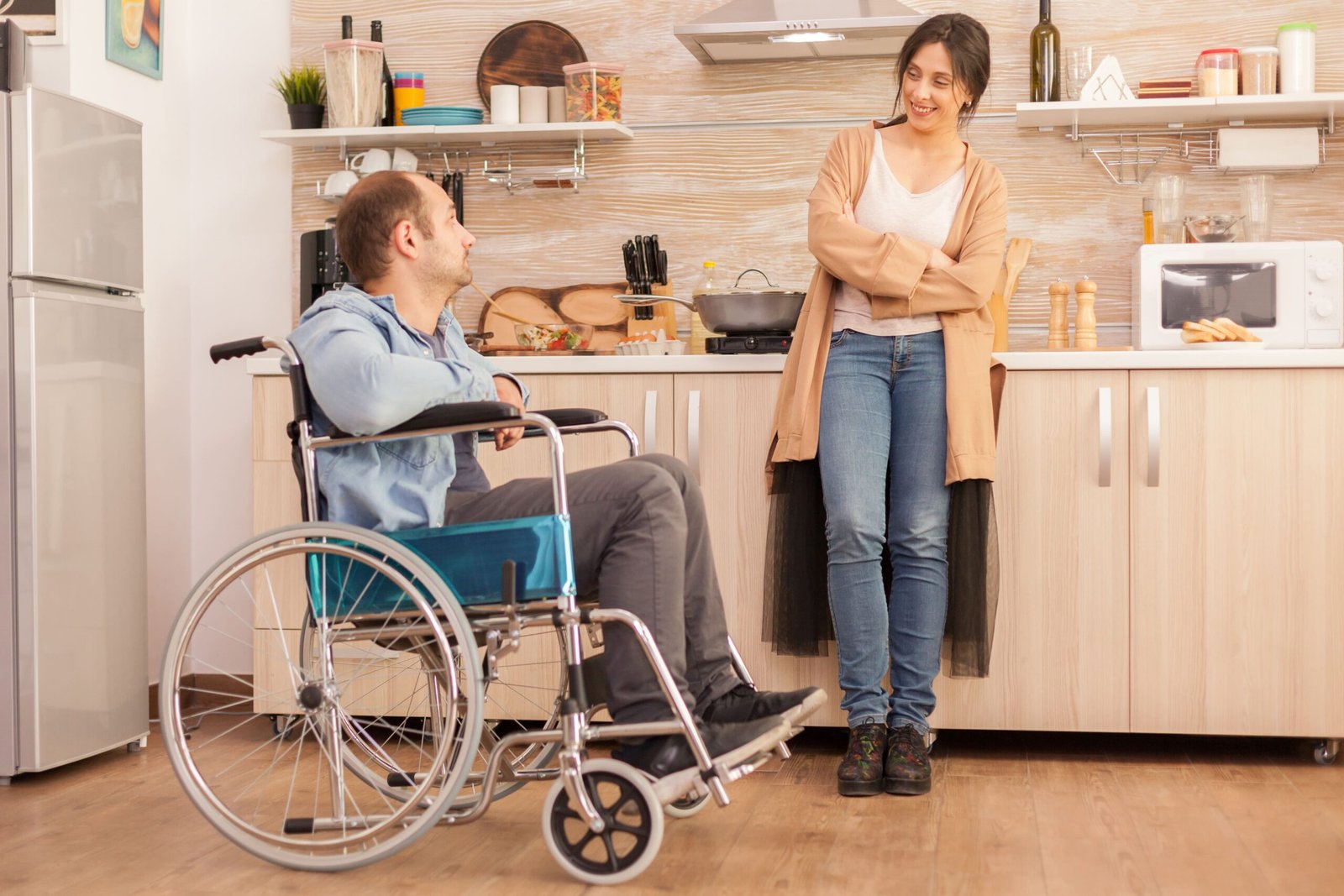 woman smiling disabled husband wheelchair while talking with him disabled paralyzed handicapped man with walking disability integrating after accident (1)